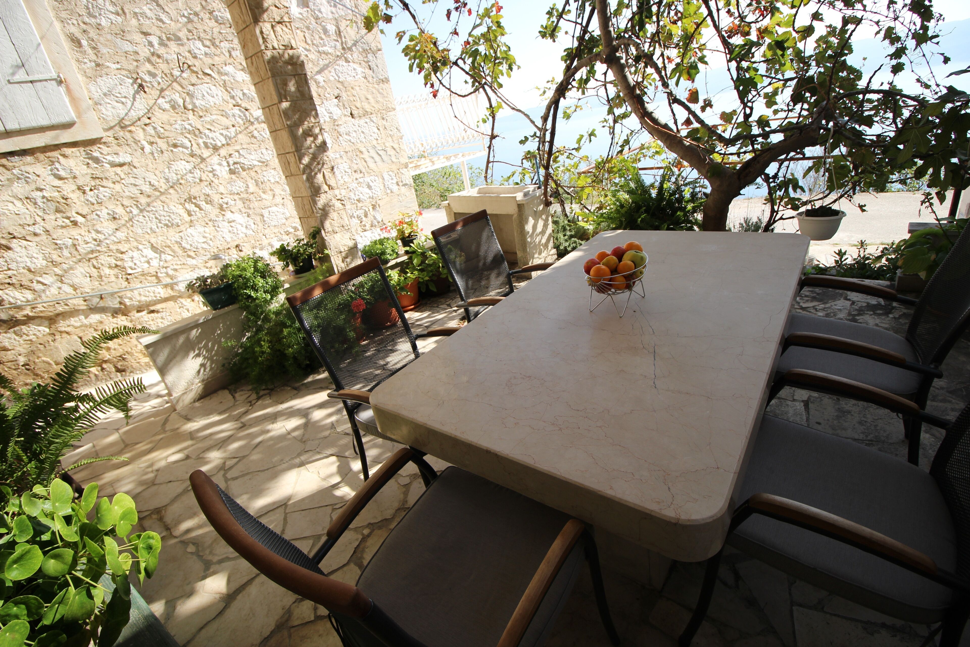 An outdoor dining area with a stone wall, potted plants, and a table with chairs.