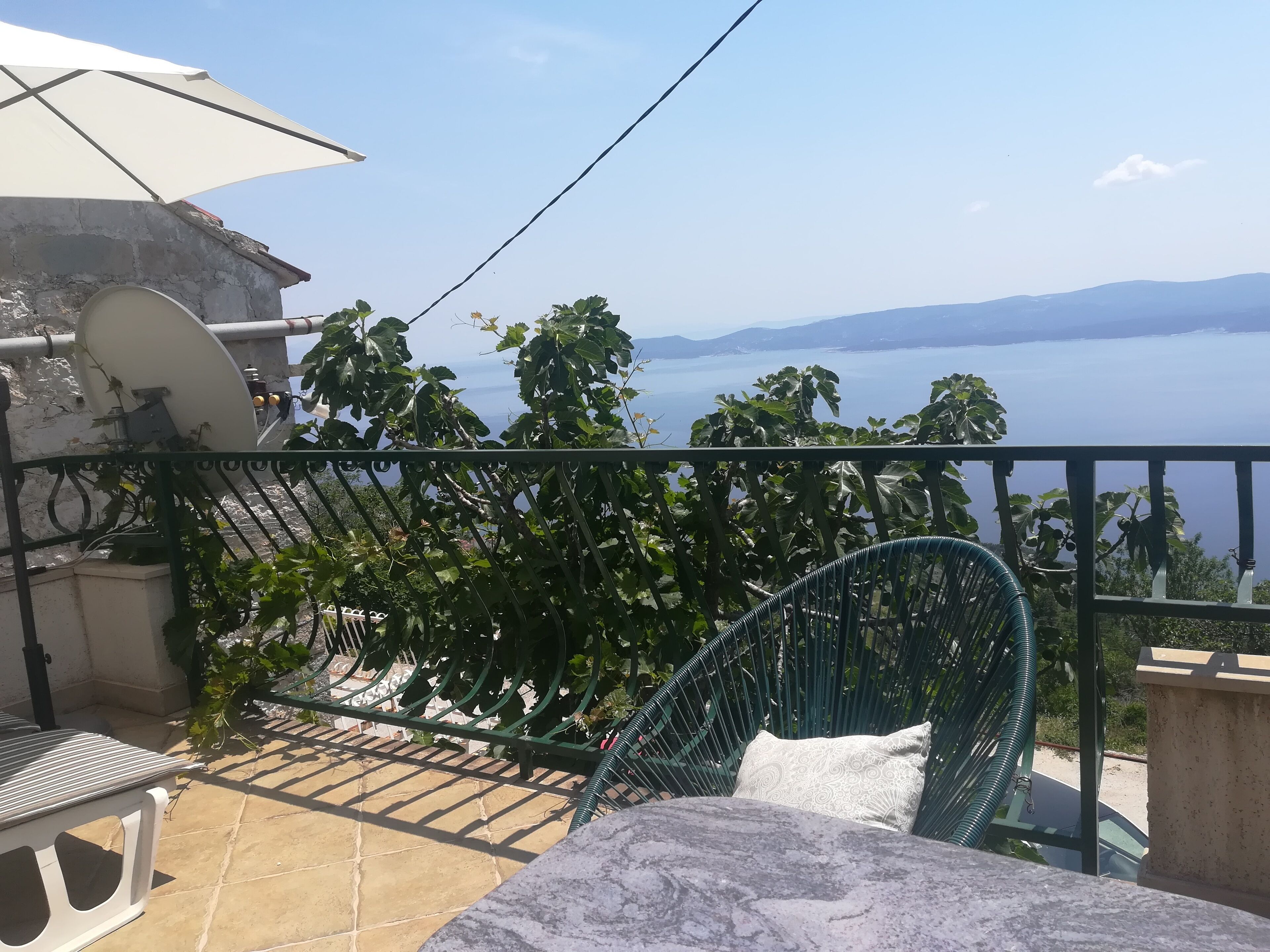 A balcony with a view of the sea, a chair, a table, and a satellite dish.
