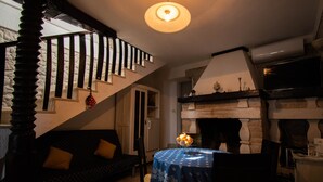 A cozy living room with a sofa, a dining table with a blue tablecloth, a fireplace, and a staircase with wooden railings. - Charming stone house with panoramic sea and mountain view (Lokva Rogoznica)
