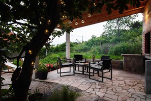 An outdoor patio area with stone flooring, black metal furniture, and string lights. - Charming stone house with panoramic sea and mountain view (Lokva Rogoznica)