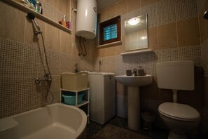 A bathroom with a bathtub, a toilet, a sink, a mirror, and a towel rack. - Charming stone house with panoramic sea and mountain view (Lokva Rogoznica)