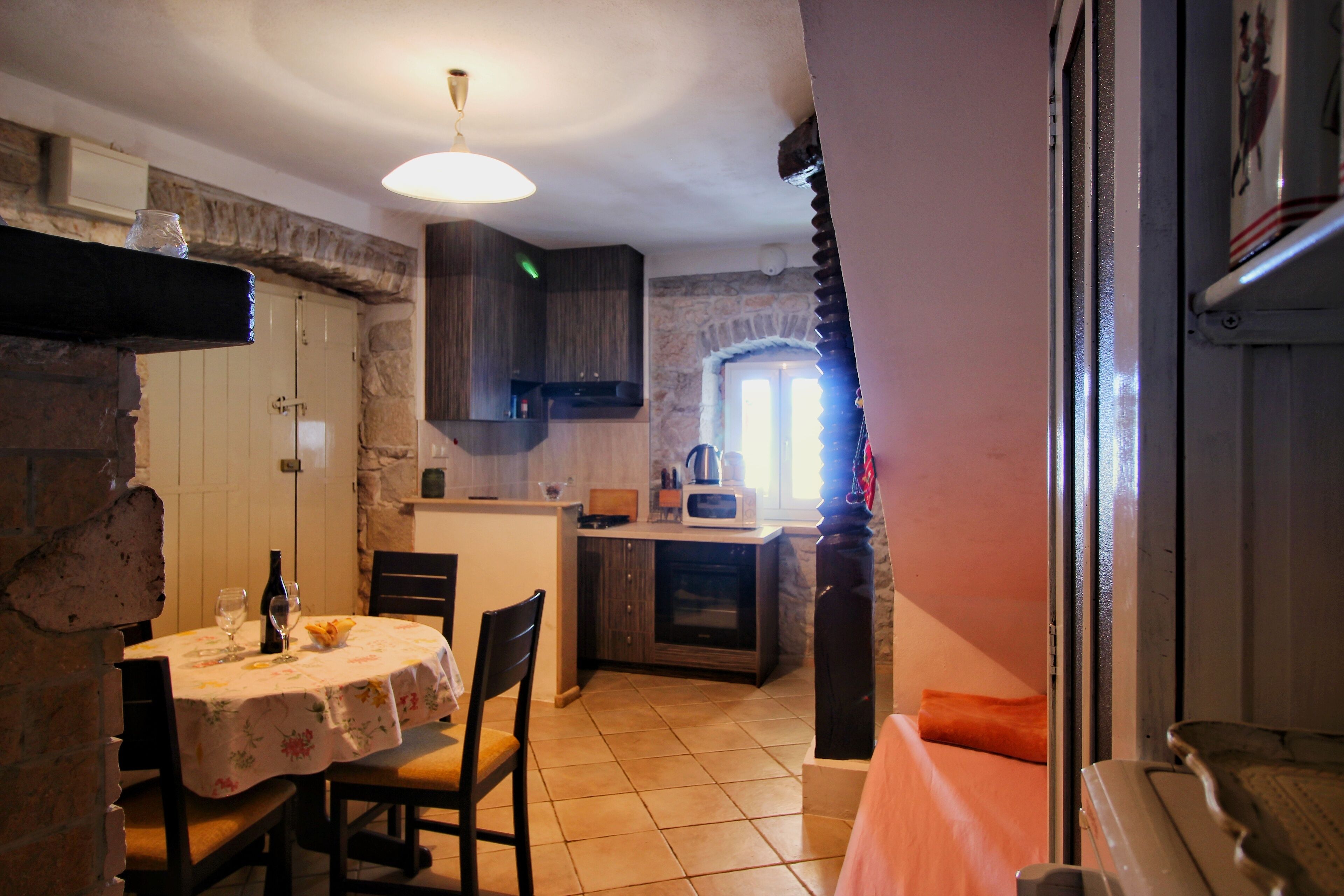 A dining area with a table set for two, a kitchen with a microwave and oven, and a stone wall.