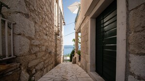 A narrow stone-paved alleyway with a view of the sea, stone walls, and a closed green door. - Charming stone house with panoramic sea and mountain view (Lokva Rogoznica)