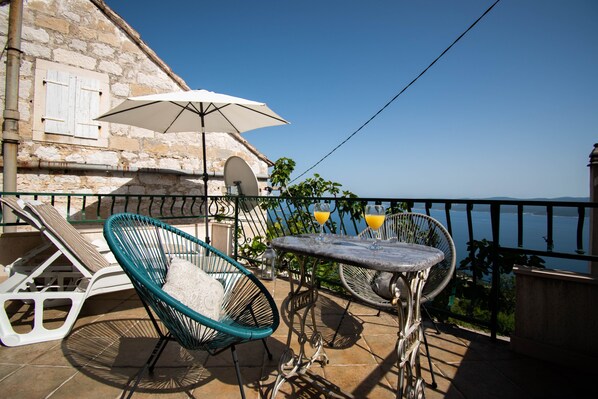A balcony with a table, two chairs, and an umbrella. - Charming stone house with panoramic sea and mountain view (Lokva Rogoznica)
