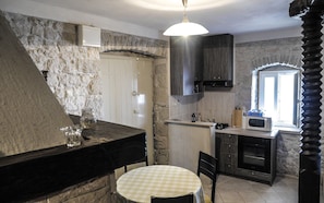 A kitchen with a stone wall, a round table, a microwave, and a hanging light fixture.