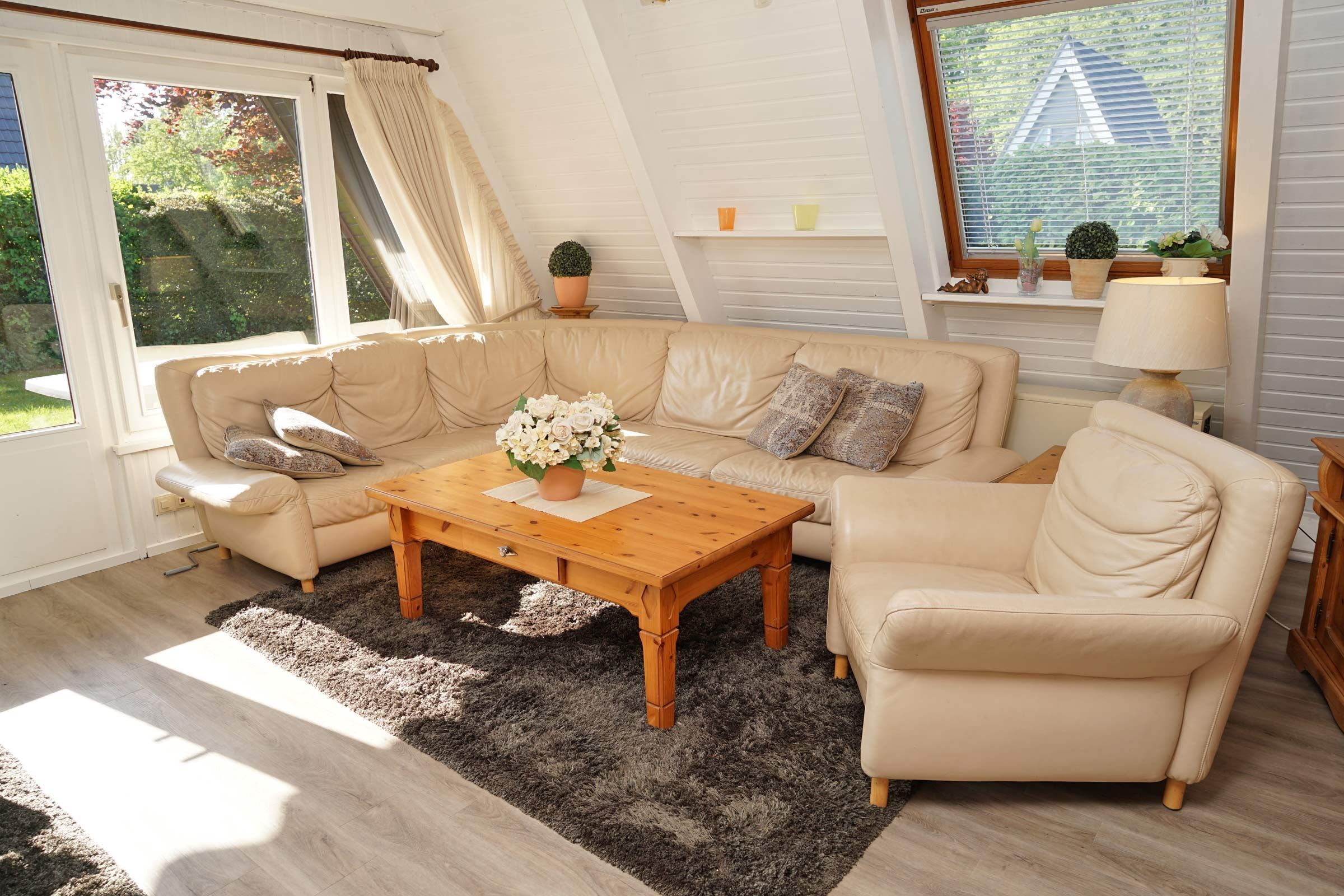 A cozy living room with a beige sofa set, a wooden coffee table, and a large window with blinds.