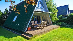 Ein modernes Haus mit Satteldach, einer Terrasse mit Tisch und Stühlen sowie einem kleinen Garten.
