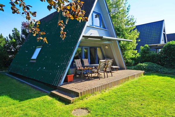 A modern house with a slanted roof, a patio with a table and chairs, and a small garden area.