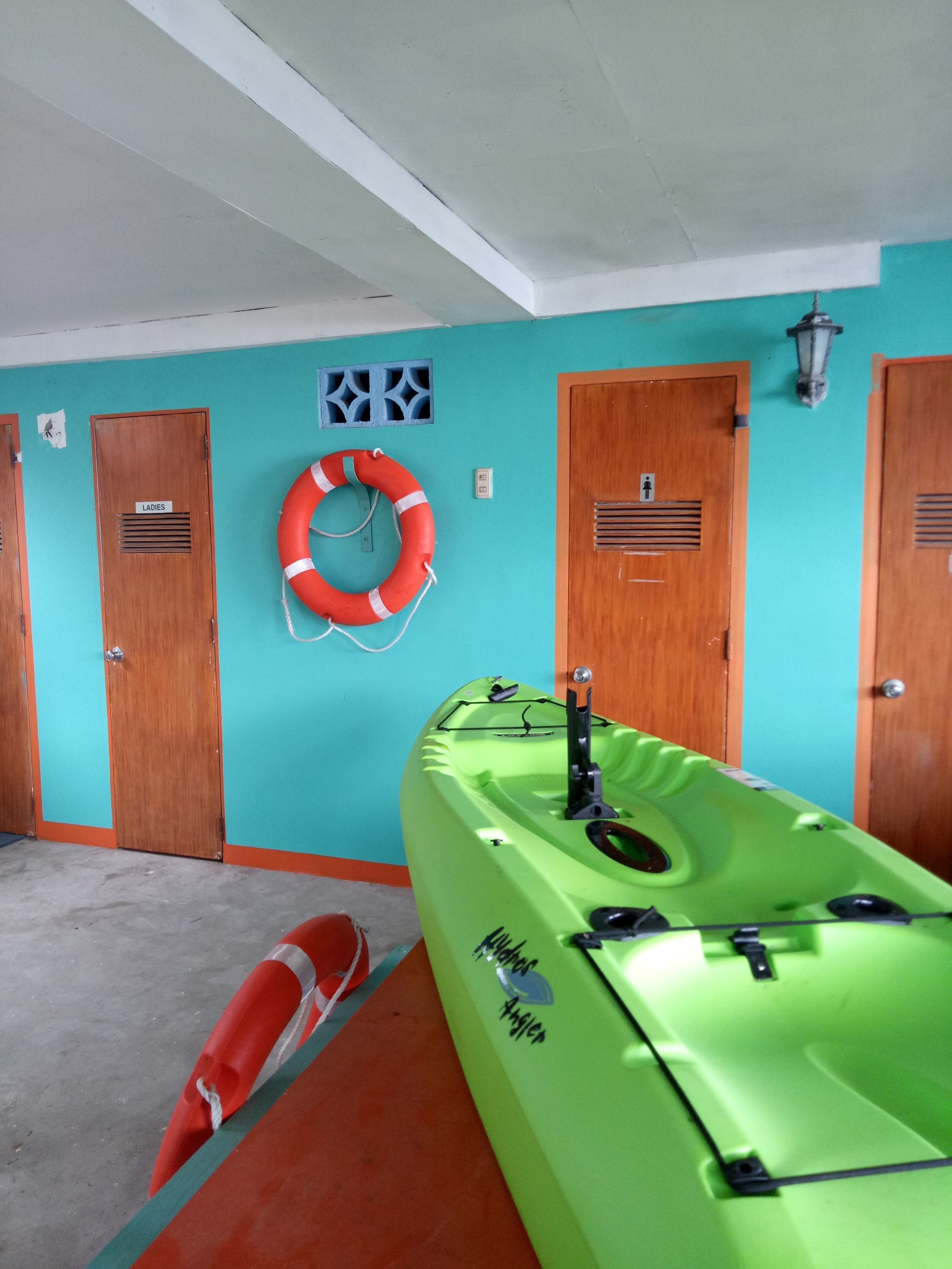 Ein Zimmer mit türkisfarbenen Wänden, Holztüren, einem grünen Kajak und einem roten Rettungsring.