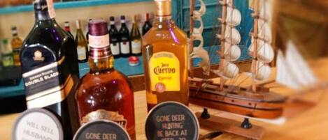 A bar counter with various bottles of alcohol, including a bottle labeled "Gone Deer Hunting Be Back at Beer: 30".