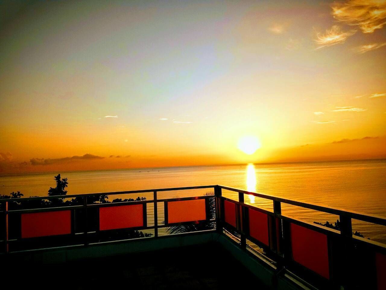 A sunset over a calm sea with a bridge in the foreground.