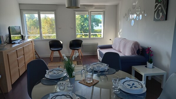 A dining area with a table set for four, two black chairs, a sofa, and a small table with a potted plant.