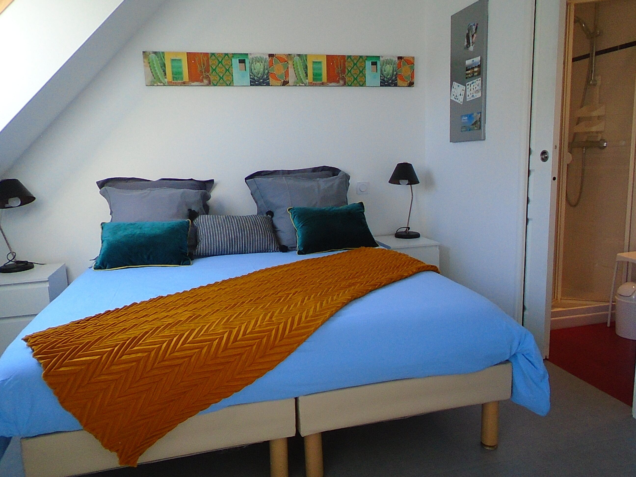 A bedroom with a bed, two nightstands, a wall art piece, and a shower area.