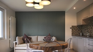 A modern kitchen with a dining area, including a wooden table, clear chairs, and a sofa with cushions.