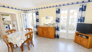 Un coin repas comprenant une table et des chaises, un meuble en bois, un téléviseur et une fenêtre avec des rideaux.