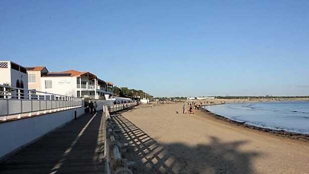 Une plage avec une promenade en bois, des bâtiments dotés de balcons et un ciel dégagé.