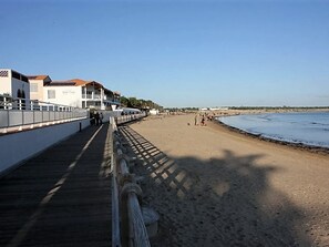 Ein Strand mit einer Holzpromenade, Gebäuden mit Balkonen und einem klaren Himmel.