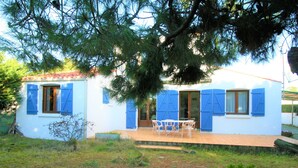 A white building with blue shutters, a patio with chairs, and a tree in the foreground.