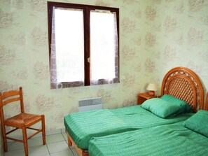 Ein Zimmer mit Bett, Stuhl, Nachttisch und einem Fenster mit Vorhängen.