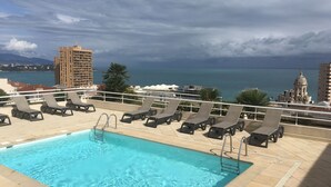 Une piscine sur le toit, dotée de chaises longues et offrant une vue sur la mer et les bâtiments.