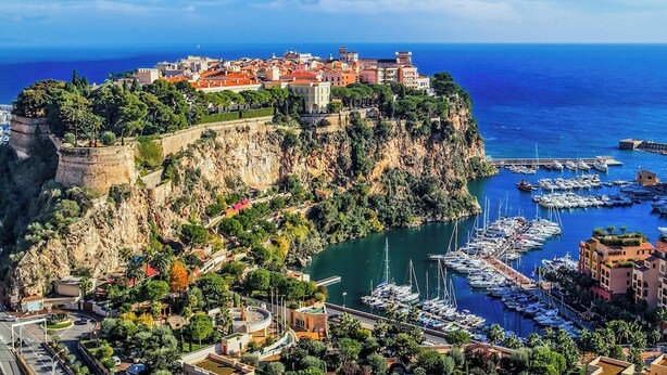 Une ville côtière dotée d’un quartier historique fortifié, situé sur une falaise, d’un port de plaisance abritant de nombreux bateaux et d’une route menant à la ville.