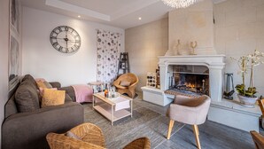 Een woonkamer met een open haard, een grote wandklok en een moderne kroonluchter.