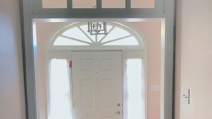 A hallway with a white door, wooden flooring, and a decorative ceiling.