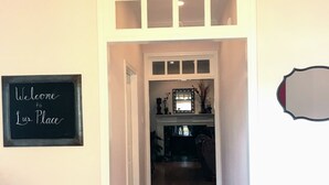 A hallway with wooden flooring, a blackboard with 'Welcome to Iris Place' written on it, and a mirror on the wall.