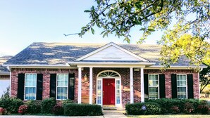 A two-story brick house with a red front door, white shutters, and a covered porch.