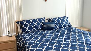 A bedroom with a bed covered in a blue and white patterned bedspread, a wooden nightstand with a telephone, and a wall-mounted cross.