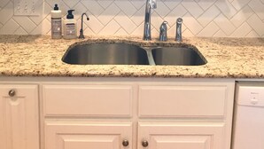 A kitchen with two sinks, white cabinets, a window, and a tiled backsplash.