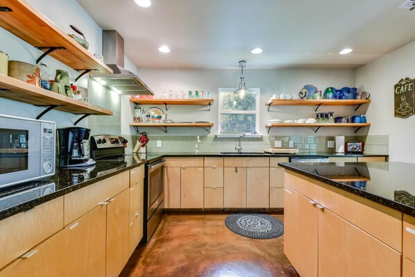 A compact kitchen with wooden cabinets, a microwave, a coffee maker, and shelves with dishes and kitchenware.
