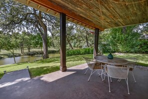 An outdoor patio with a table and chairs, a pergola overhead, and a view of a pond and trees.