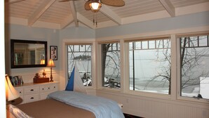 Ein Schlafzimmer mit Bett, Deckenventilator, Fenster mit Blick auf eine verschneite Landschaft und einem Schminktisch mit Lampe.