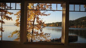 Ein Zimmer mit großem Fenster und Blick auf einen See sowie Herbstlaub.