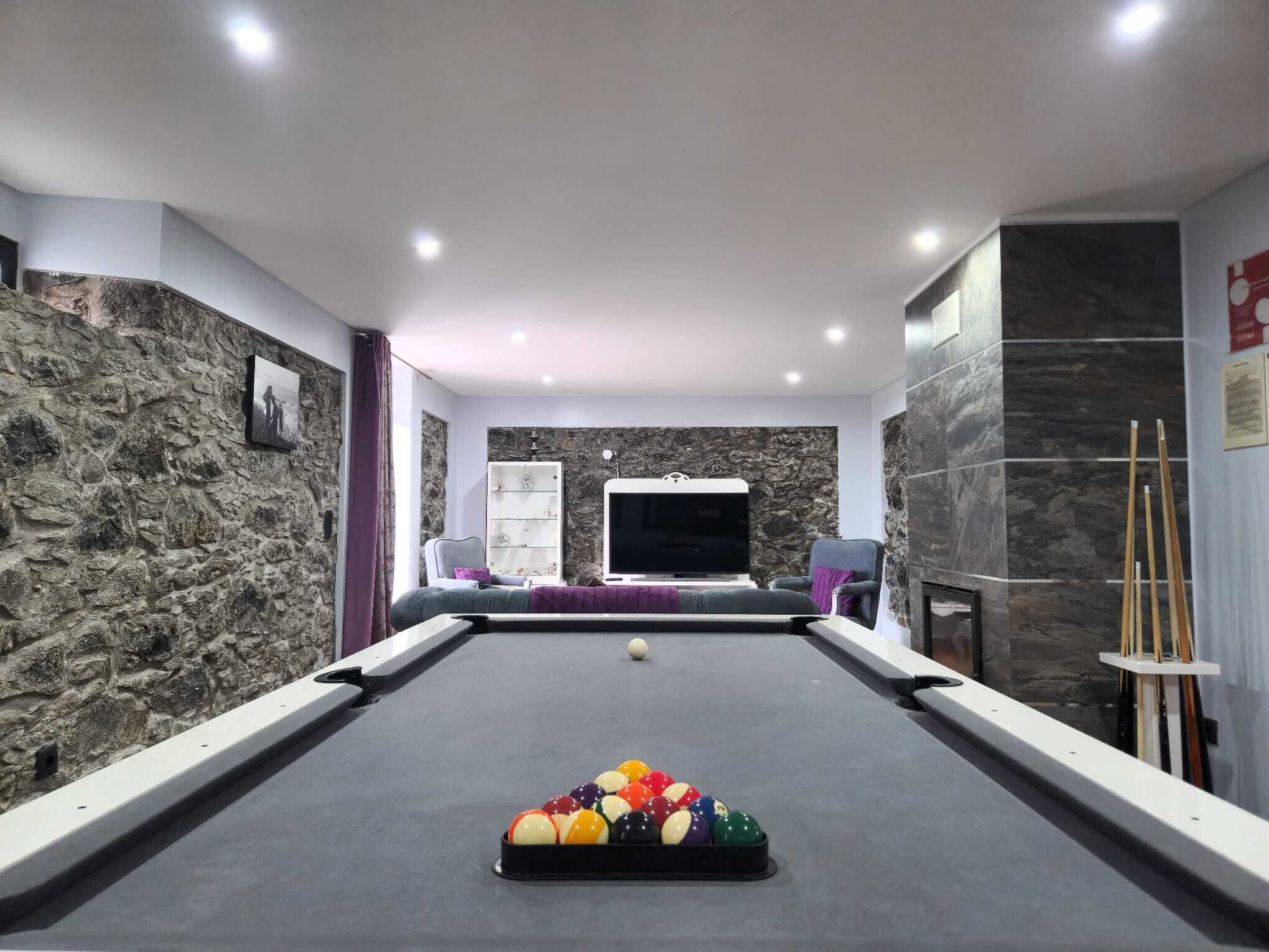 A pool table with balls, a television, and a stone wall.