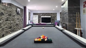 Een pooltafel met ballen, een televisie en een stenen muur.