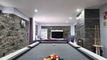 A pool table with balls, a television, and a stone wall.