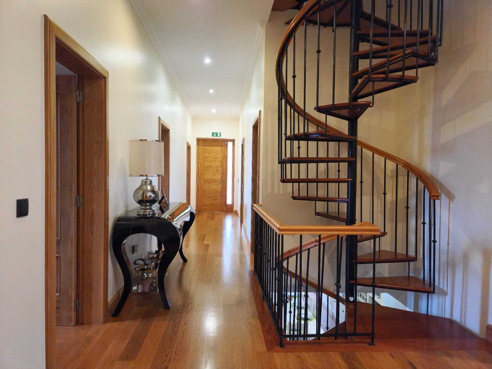 A hallway with a wooden floor, a desk with a lamp, and a spiral staircase.