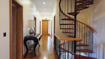 A hallway with a wooden floor, a desk with a lamp, and a spiral staircase.