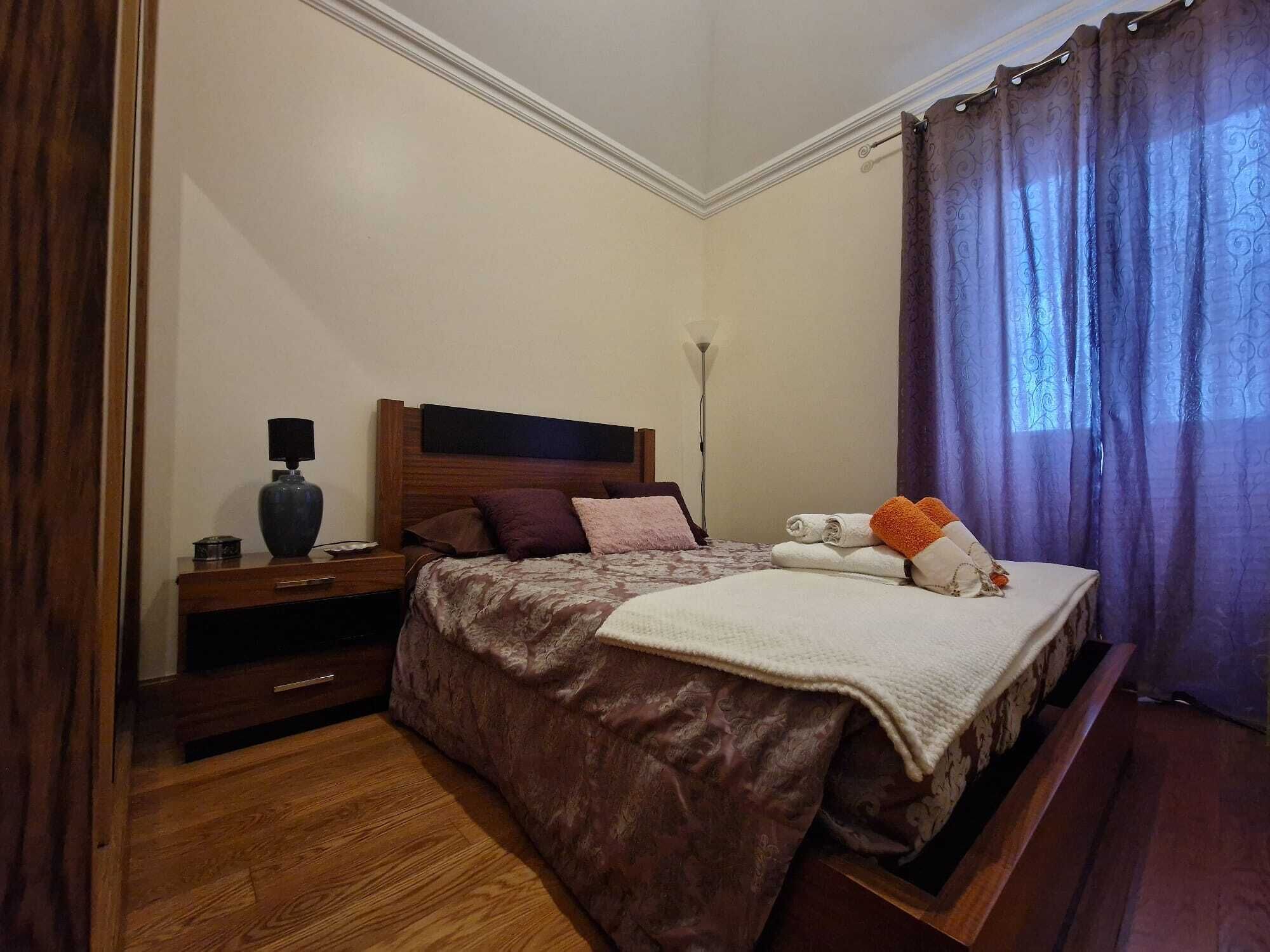 Ein ordentlich eingerichtetes Schlafzimmer mit Bett, Nachttisch, Lampe und Vorhängen.