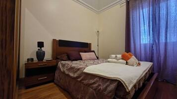 Ein ordentlich eingerichtetes Schlafzimmer mit Bett, Nachttisch, Lampe und Vorhängen.