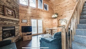 Ein gemütliches Blockhaus-Interieur mit Kamin aus Stein, Holzwänden, einem Essbereich und einer Treppe.