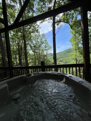 Een hottub omgeven door een houten terras, met uitzicht op een bos.
