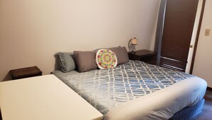 Ett sovrum med en säng, ett sängbord, en lampa och en dörr.
