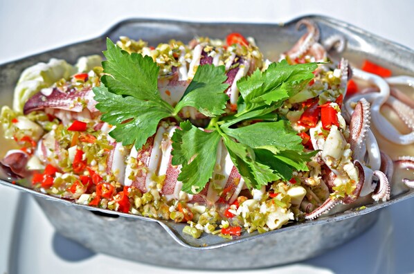 A seafood dish with octopus, red peppers, and herbs in a metal serving dish.