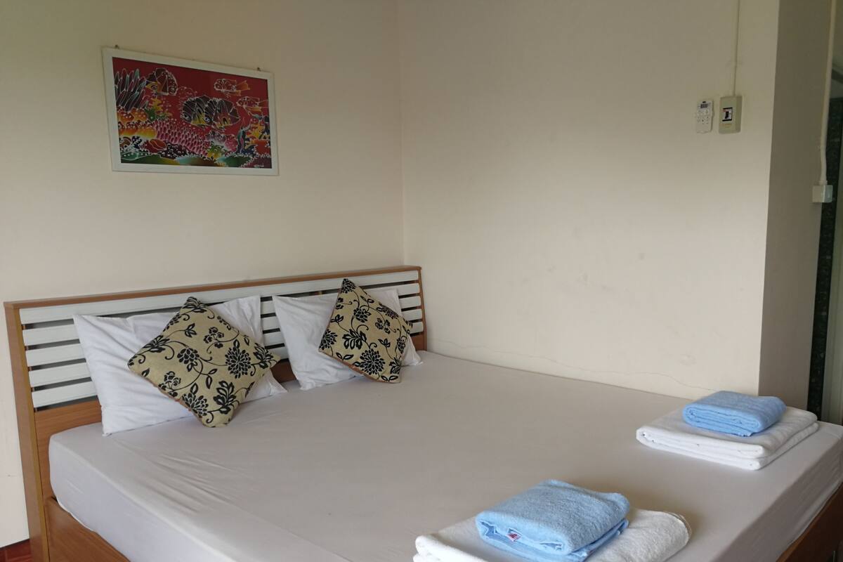 A bed with a wooden frame, white bedding, patterned pillows, and a folded blue towel on the side.