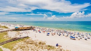 Een strand met vele parasols en ligbedden, een pier op de achtergrond en een heldere lucht.