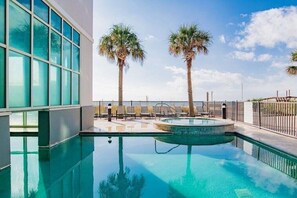 Ein Schwimmbad mit zwei Palmen, einer umzäunten Terrasse und einem Gebäude mit großen Fenstern.