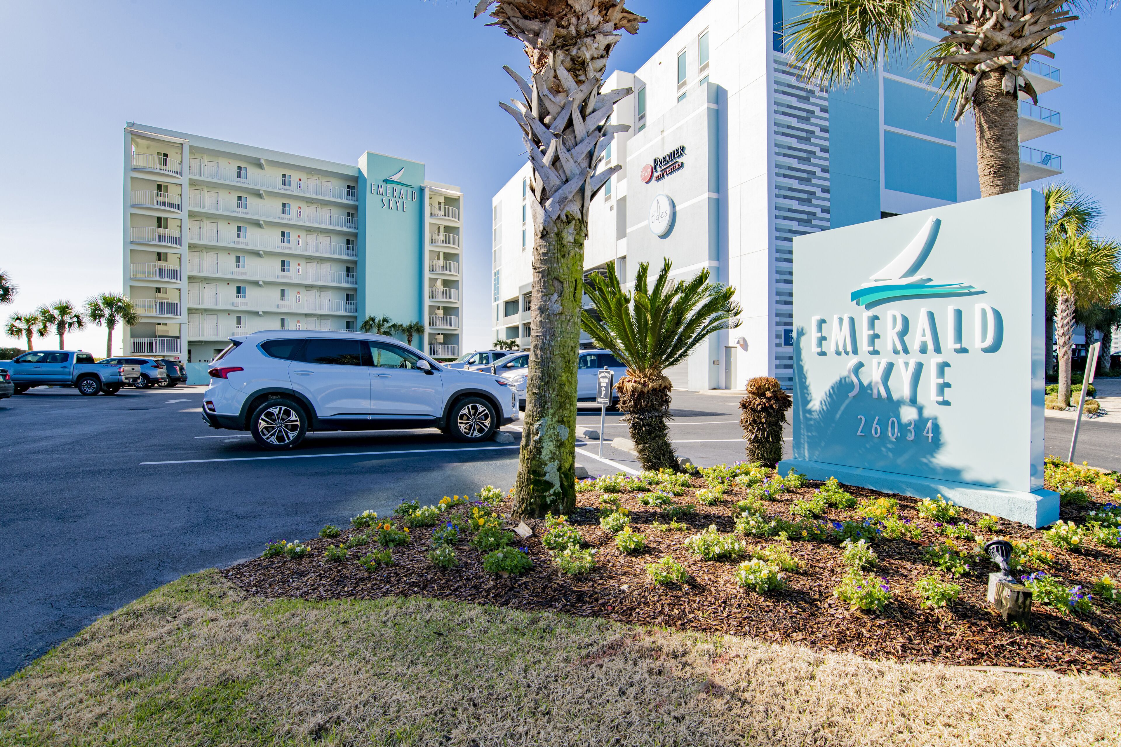 Ein Hotelschild mit dem Logo eines Segelboots, umgeben von Palmen und einem Parkplatz mit Autos.